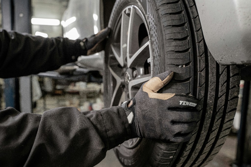 Mechaniker mit Arbeitshandschuhen montiert einen Reifen an einem Fahrzeug in der Werkstatt